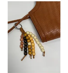 Détail de sac cabas tressé marron avec un pendentif décoratif en perles de bois