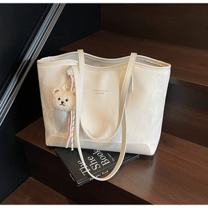 Detail of white PU leather tote bag with plush bear charm and textured finish