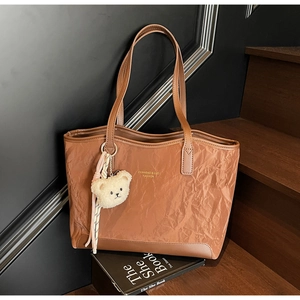 Detail view of brown tote bag featuring unique pleated texture and plush bear charm