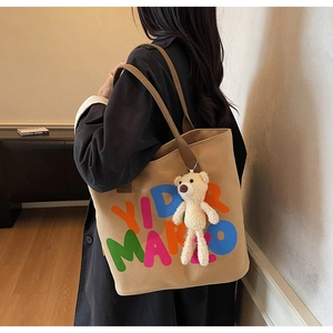 Detail view of khaki canvas tote with artistic letter print and a plush bear pendant