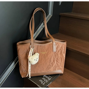 Detail of dark brown tote bag with wrinkled texture, leather trim and a bear charm