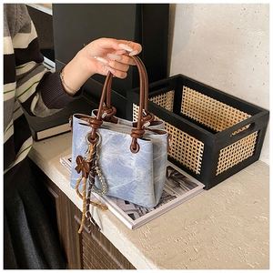 Detail of light blue bucket bag with brown knotted handles and bow charm accessory
