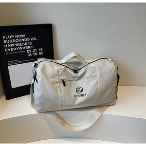Detail view of cream travel bag with NINGJIA logo, front pocket, and adjustable strap