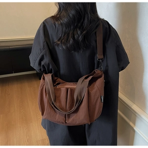 Detail of a brown crescent-shaped pleated bag with adjustable wide strap and woven label