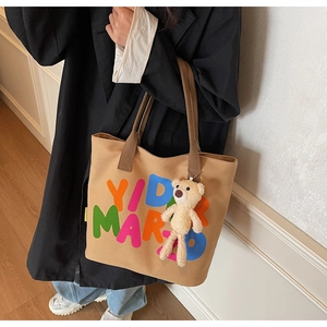 Detailed close-up of khaki canvas tote bag with colorful letters and plush bear charm