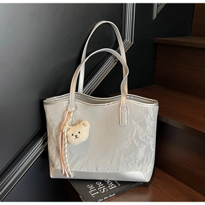 Detail of silver metallic tote bag featuring pleated texture and a plush bear charm