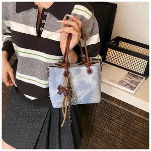 Detail of light blue washed texture tote bag with brown leather handles and bow charm
