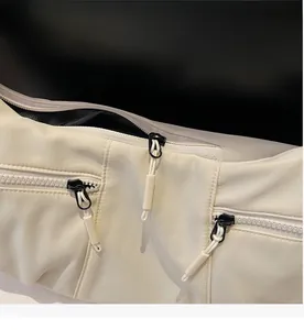 Close-up of smooth black zippers with white pull cords on a beige nylon crossbody bag