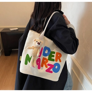 Detail of white canvas tote bag with IDER MARZO print and plush bear charm accessory