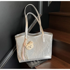 Detail of silver tote bag featuring pleated texture and cute plush bear charm