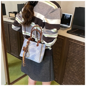 Fashionable denim bucket bag with brown leather handles and decorative charm details