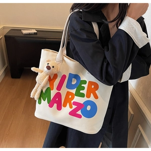 Detail of canvas tote bag with colorful letters and a cute bear plush keychain