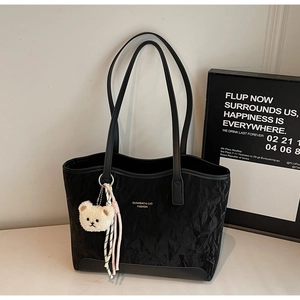 Detail of black pleated tote bag showing brand lettering and cute bear plush charm