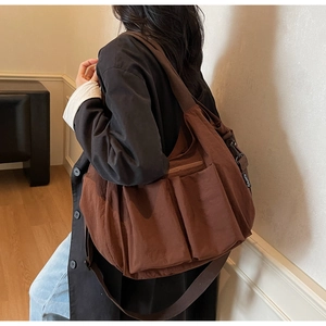 Detail of dark brown crossbody tote bag with multi-pocket design and pleated nylon texture