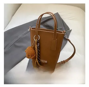 Détail du sac seau marron en cuir mat avec pendentif ours et garniture en foulard soie