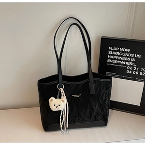 Detail of a large black tote bag with quilted texture and a cute white bear keychain