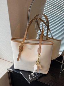 Large white faux leather tote bag with brown straps and elephant charm in interior setting