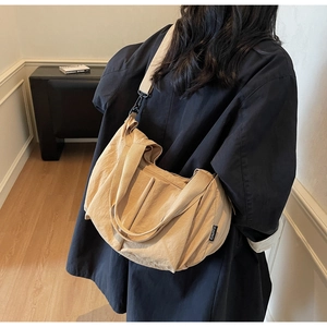 Detail of a large beige crossbody bag with adjustable wide strap and black RANATU label