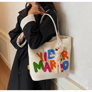 Detail of white canvas tote bag with YIDERMARZO lettering and plush bear charm