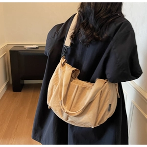 Detail view of beige canvas tote bag with wide strap being worn as a crossbody by model