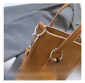 Détail du crochet argenté et de la sangle tissée du sac de téléphone en daim brun