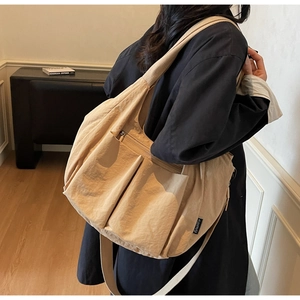 Side view of large beige crossbody tote bag with pocket and brand label on a model