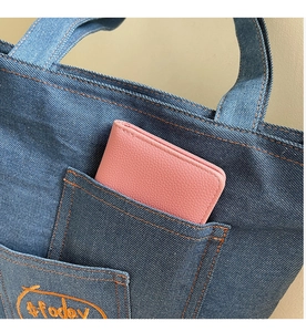Close-up of a pink pebbled leather wallet tucked inside a denim tote bag pocket