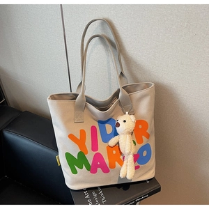 Close-up of off-white canvas tote with colorful lettering and cute plush bear charm