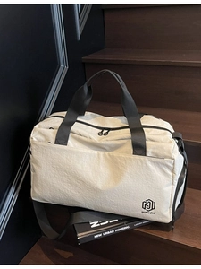 Large beige travel duffel bag with black straps on a modern dark wooden stairs background