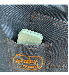 Close-up of a mint green metal tin for throat lozenges inside a blue denim jacket pocket