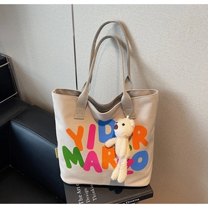 Detail of beige canvas tote bag featuring colorful letter prints and cute plush bear charm