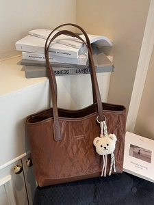 Brown textured tote bag with dark brown trim and plush bear charm in a home setting