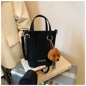 Macro shot of black bucket bag with silver metal plaque and plush teddy bear charm detail