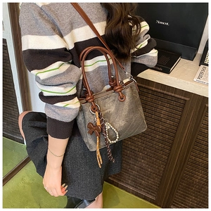 Detail of gray retro bucket bag with brown bow, braided rope and beaded pendant decoration