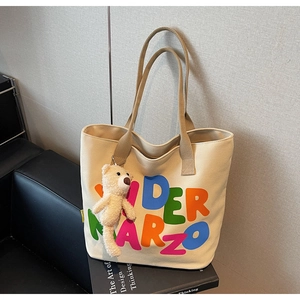 Detail of canvas tote bag with colorful letters and a cute plush bear charm accessory