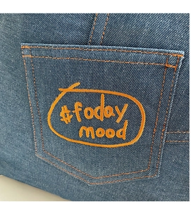 Close-up of blue denim tote bag featuring orange #foday mood embroidery and stitching