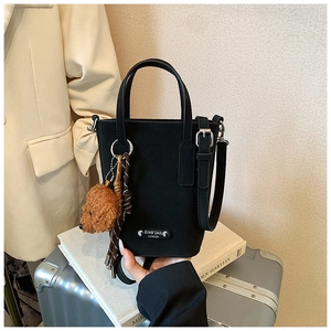 Detail of black crossbody bucket bag with brown teddy bear charm and silver hardware