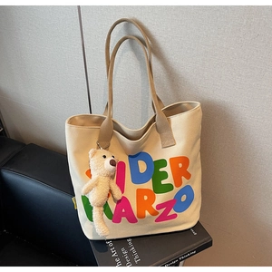Detail of canvas tote bag with colorful letters and plush bear charm on design books