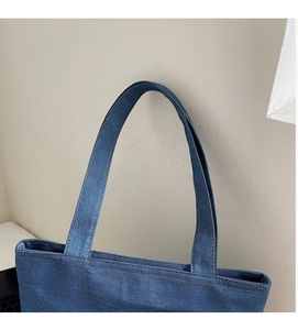 Detail of blue denim tote bag showing brown stitching and sturdy double handles