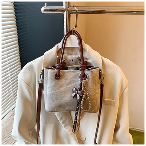 Close-up of gray vintage bucket bag with brown handles and decorative beaded chain charm