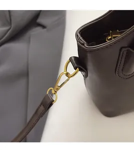 Detail of dark brown leather bag showing golden metal hook and detachable strap system