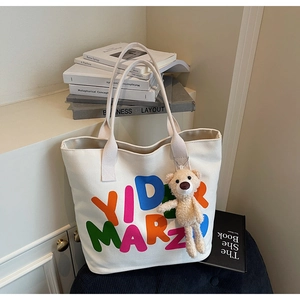 Detail of white canvas tote bag with YID MARZO print and a cute brown plush bear charm