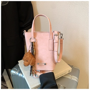 Pink matte leather bucket bag with teddy bear charm and metal logo on a silver suitcase