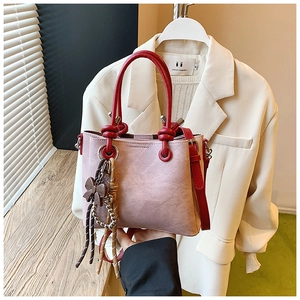 Detail of a dusty pink leather bucket bag featuring red handles and a brown bow charm