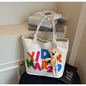 Detail of white canvas tote bag with colorful YID MARZO print and plush bear charm