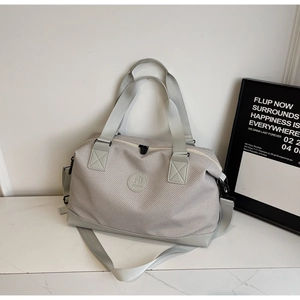 Close-up of a light grey duffel bag with woven texture, round logo, and detachable strap