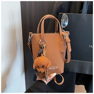 Brown PU leather bucket bag detail with metal logo nameplate and plush teddy charm