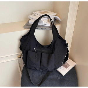 Detail of black nylon tote bag with dual front pockets and woven shoulder strap