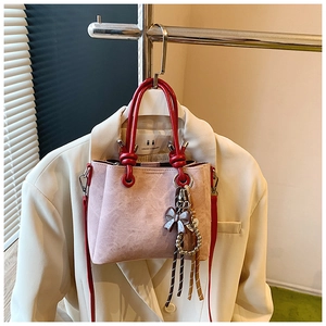 Detail of pink matte bucket bag featuring a red circular handle and brown bow charm