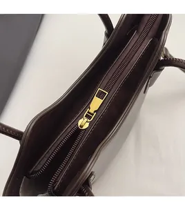 Detailed close-up of smooth brown leather handbag featuring a durable gold metal zipper